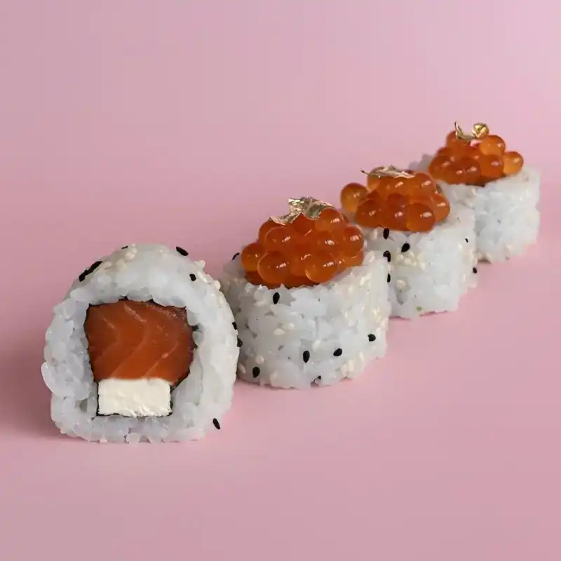 Sesame rolls with salmon and cream cheese, topped with salmon roe and gold leaf, on a pink background