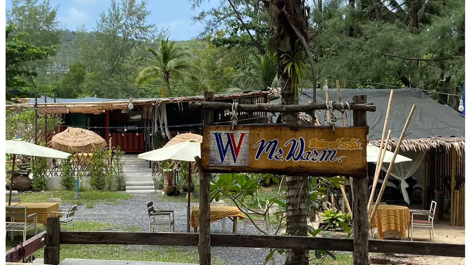 The hand-painted Mr.Warm sign at the garden gate, with tables and parasols behind it