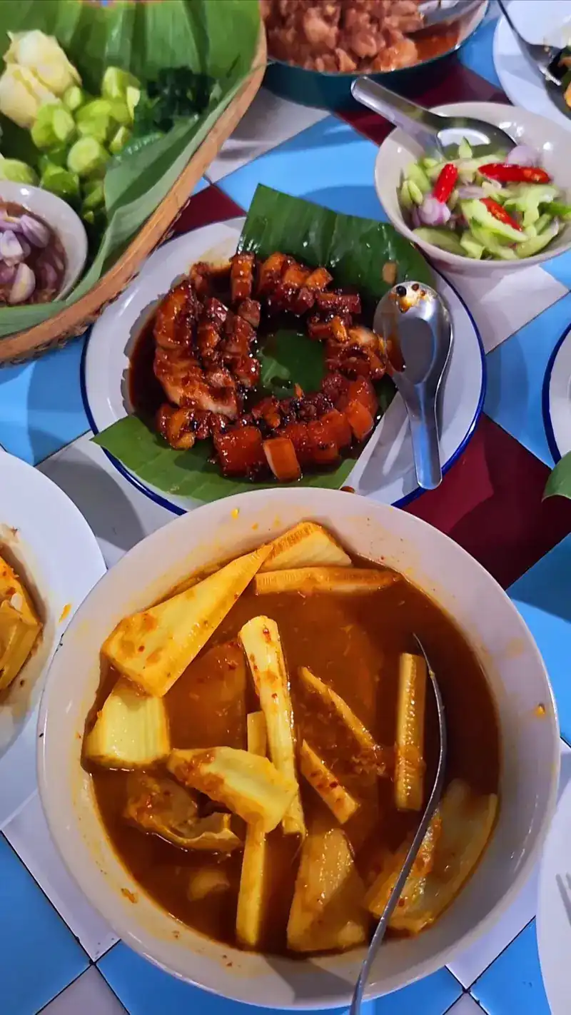 A table from above: sour curry, glazed pork on banana leaf and fresh vegetables