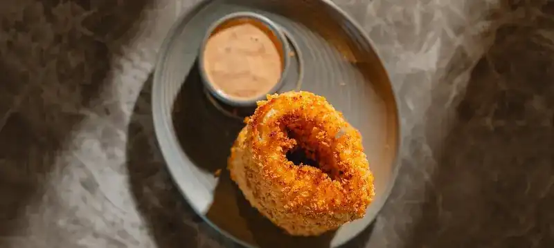 A crumbed onion ring with chipotle mayonnaise on a grey plate