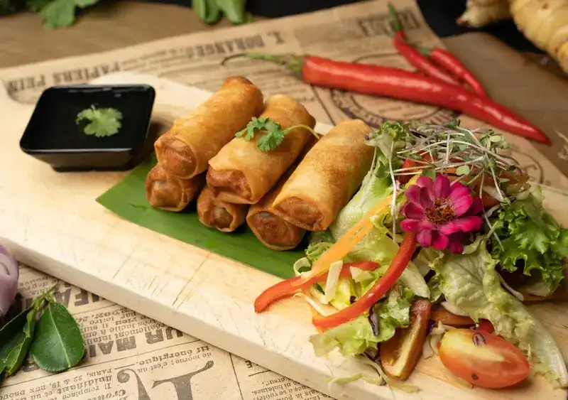 Fried spring rolls on a banana leaf with salad, on a wooden board over old newsprint