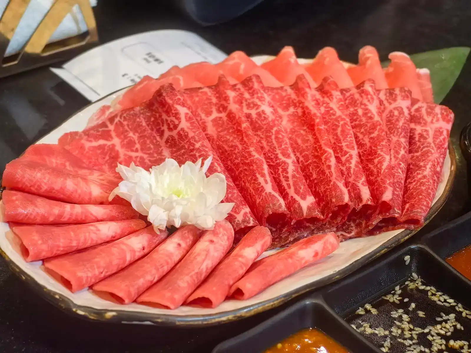 Marbled wagyu slices fanned on a plate, with dipping sauces beside it