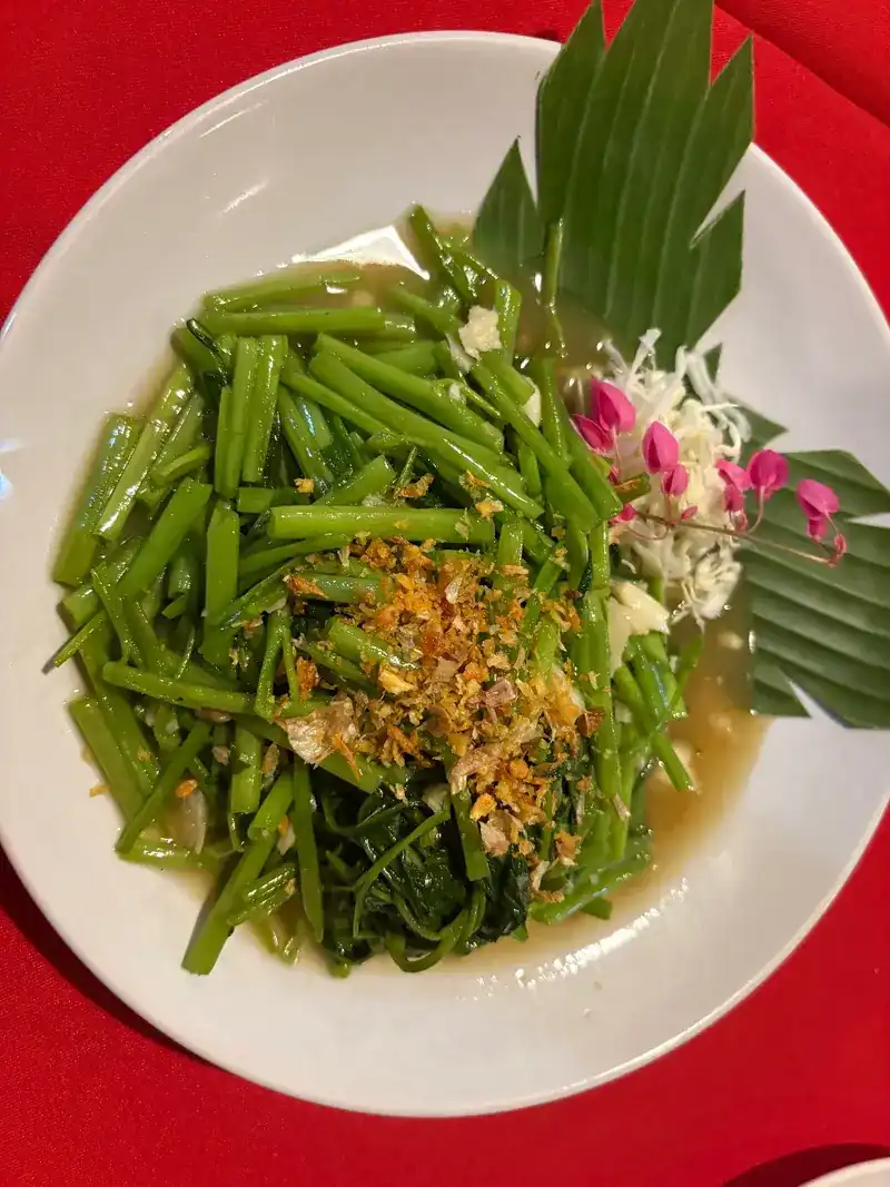 Stir-fried morning glory topped with fried garlic, with a cut-leaf fan and pink flowers