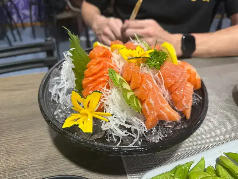 Slices of salmon sashimi on crushed ice with shredded radish, a green leaf and carved yellow flowers