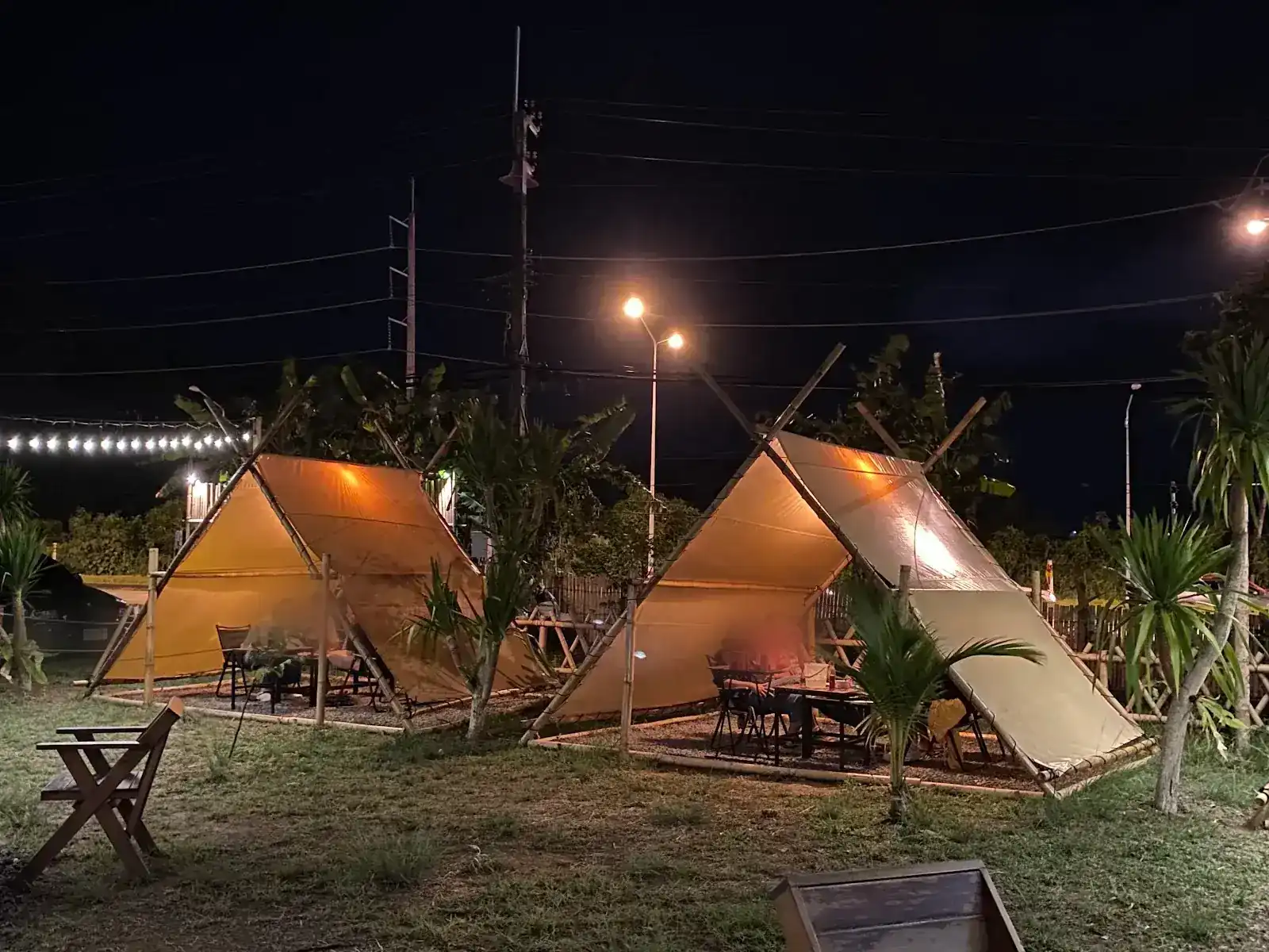 Two canvas A-frame tents lit up at night on the lawn, each with a table inside