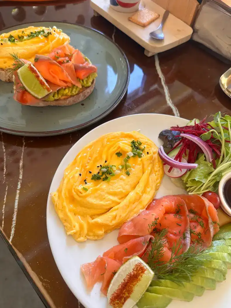 Scrambled eggs with smoked salmon, avocado and salad, a salmon toast behind