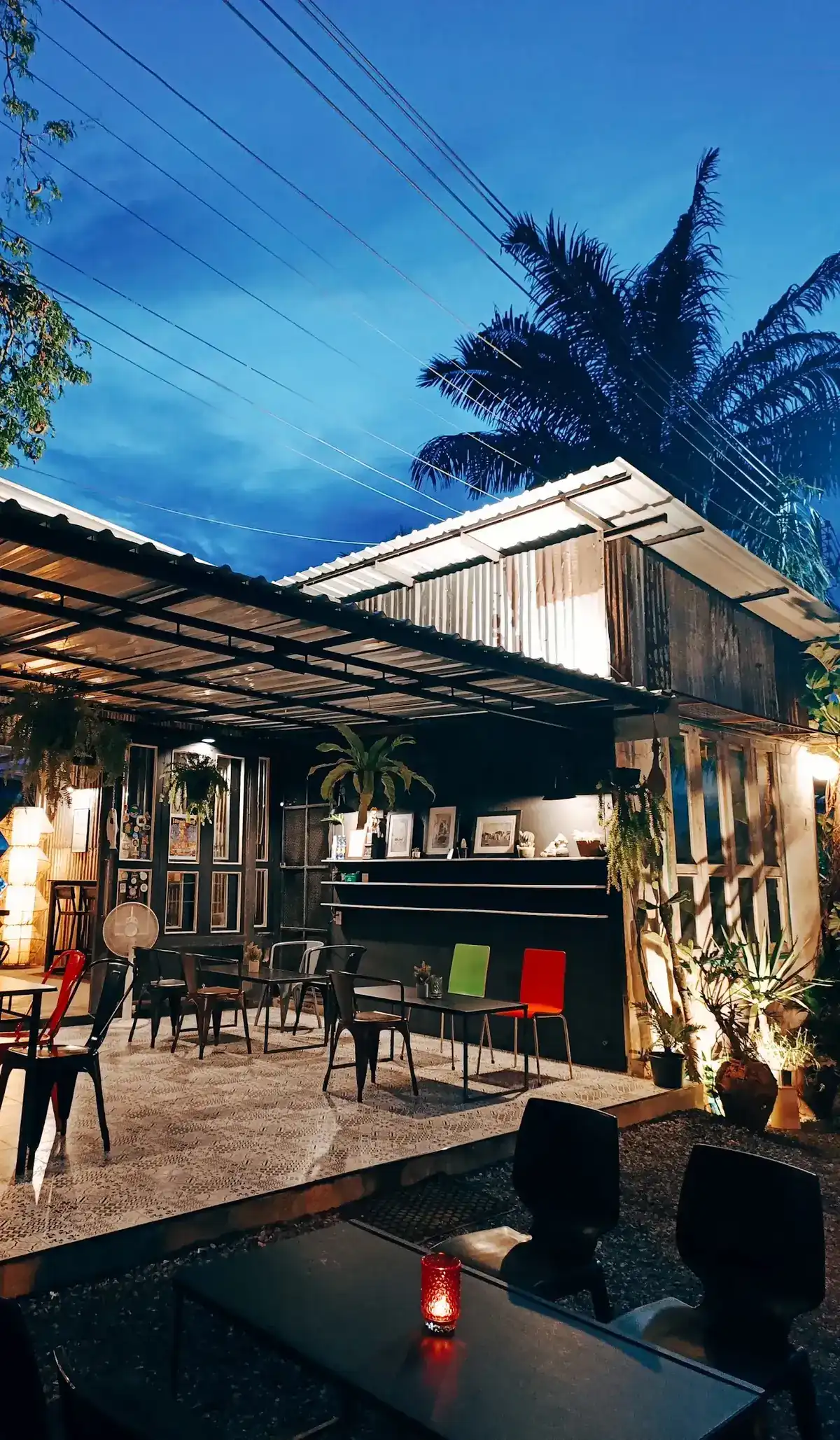 The terrace at dusk: a tin roof, red and black metal chairs on patterned floor tiles, palm trees against a deep blue sky