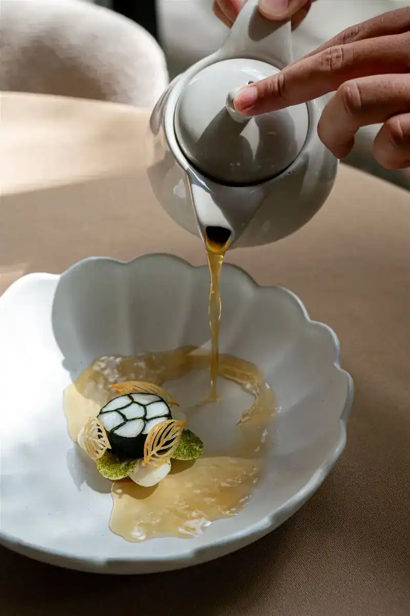 Golden broth poured from a white teapot into a scalloped bowl