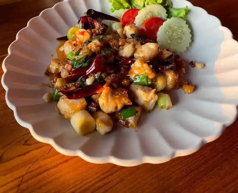 A stir-fry with dried chillies and spring onion on a fluted white plate