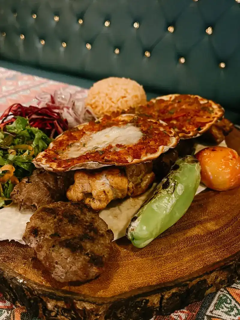 A mixed grill platter on a wooden board in front of a teal banquette