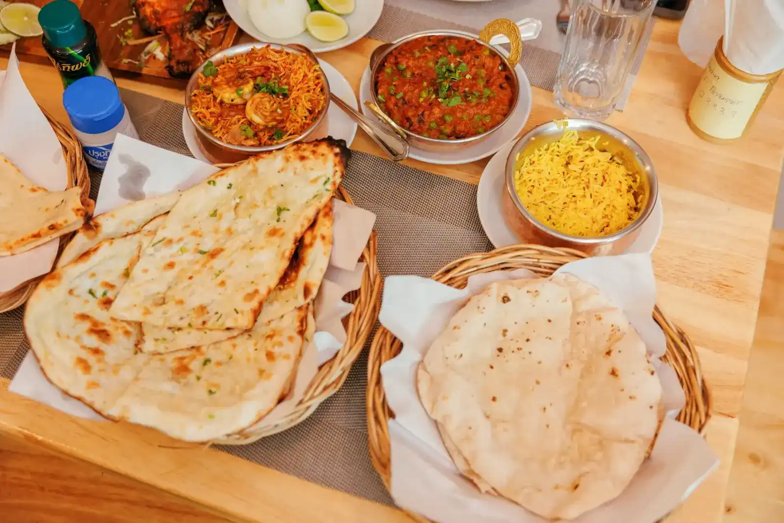 Naan and roti in baskets beside biryani, curry and saffron rice on a wooden table