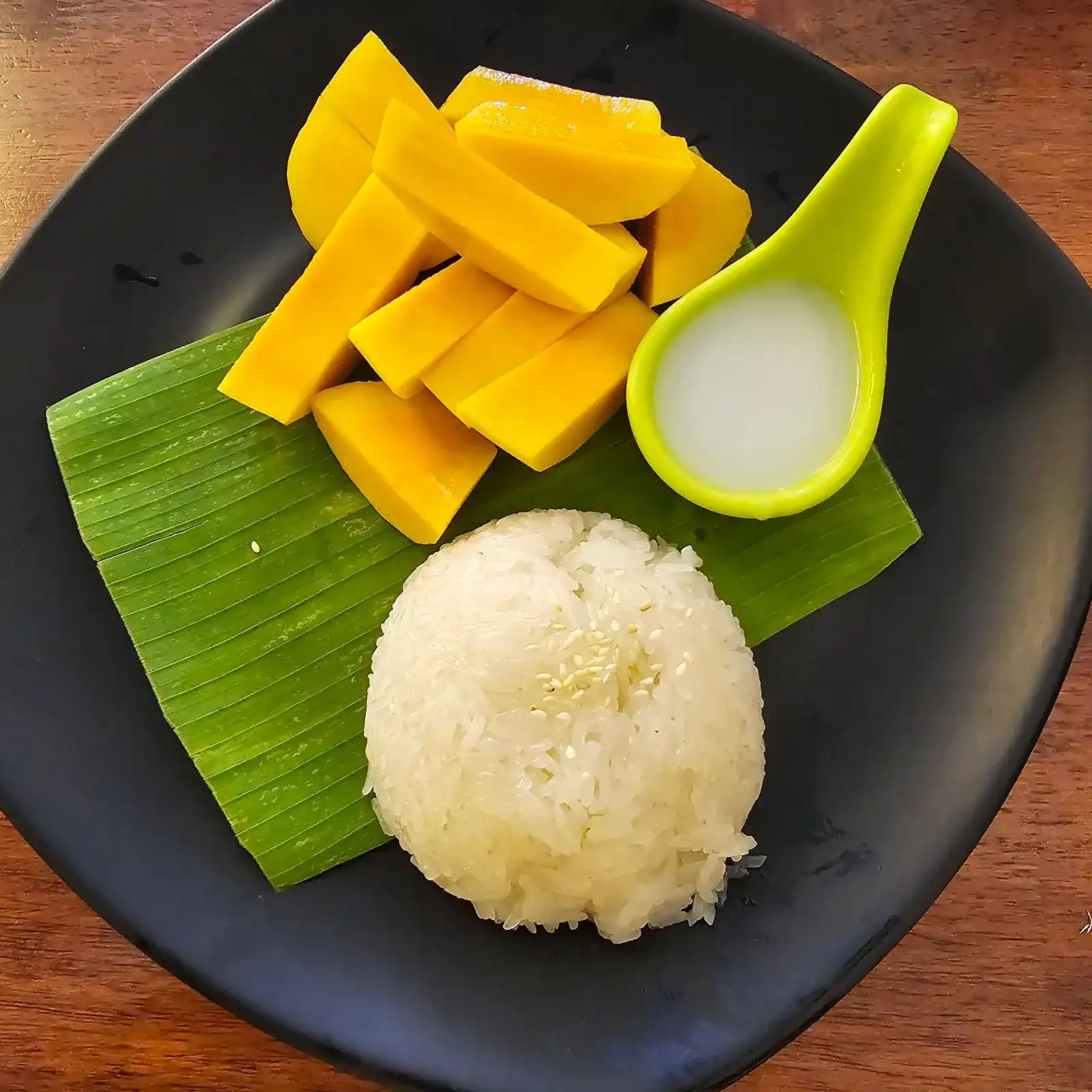 Ripe mango with sticky rice on a banana leaf, coconut cream on the side