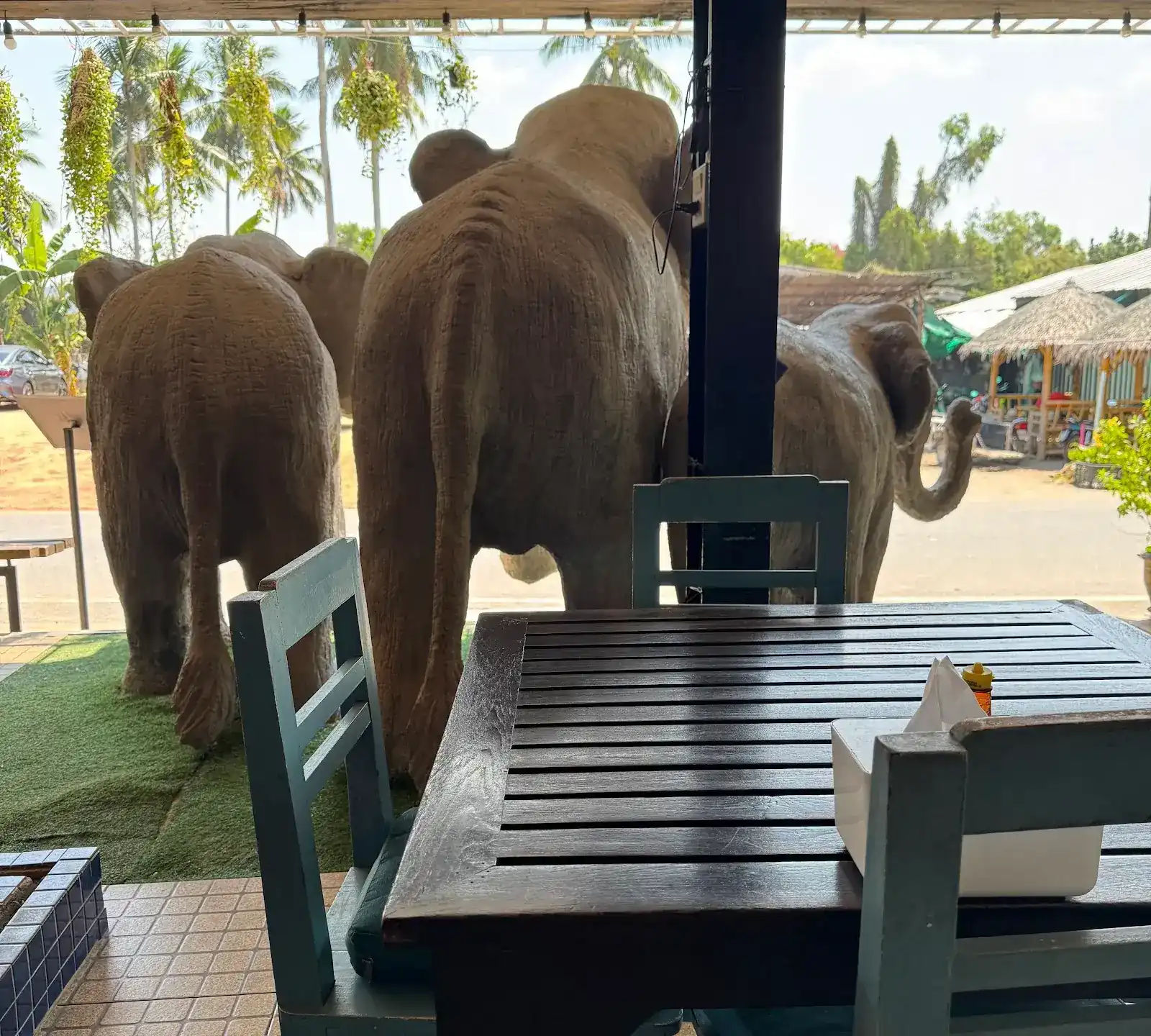 Elephant statues at the edge of the terrace, seen past an empty table and teal chairs