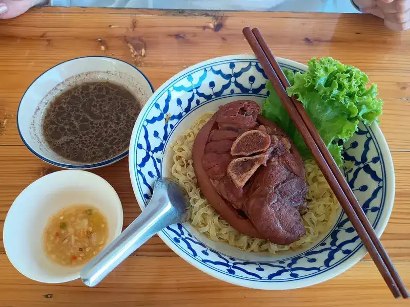Braised pork on egg noodles, with lettuce, a small bowl of broth and a dipping sauce
