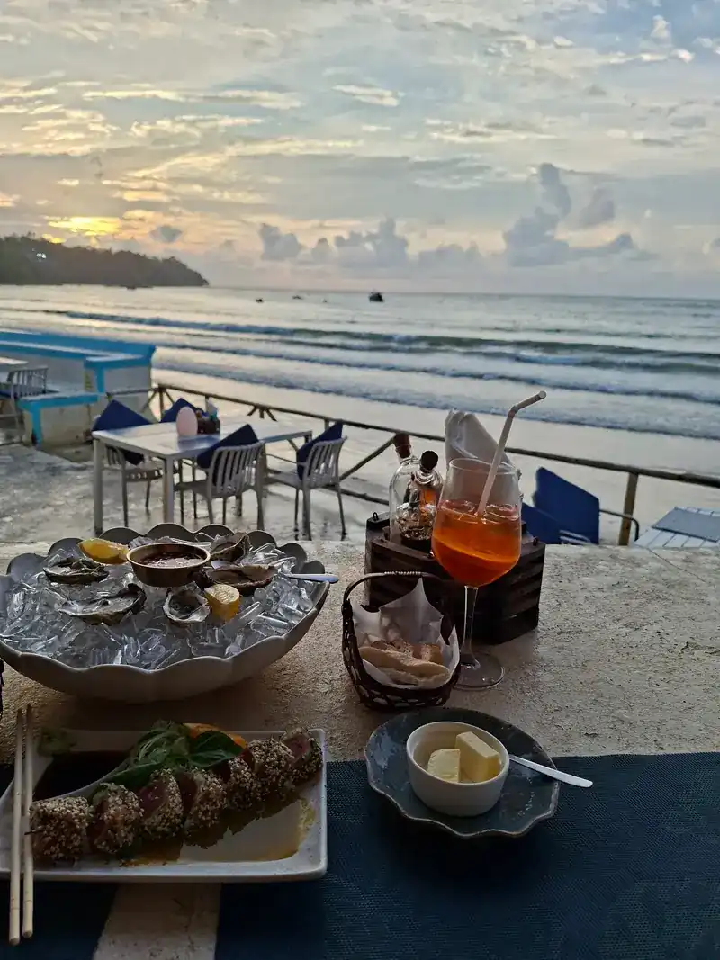 Oysters on ice and a sesame-crusted dish on a seaside table at sunset
