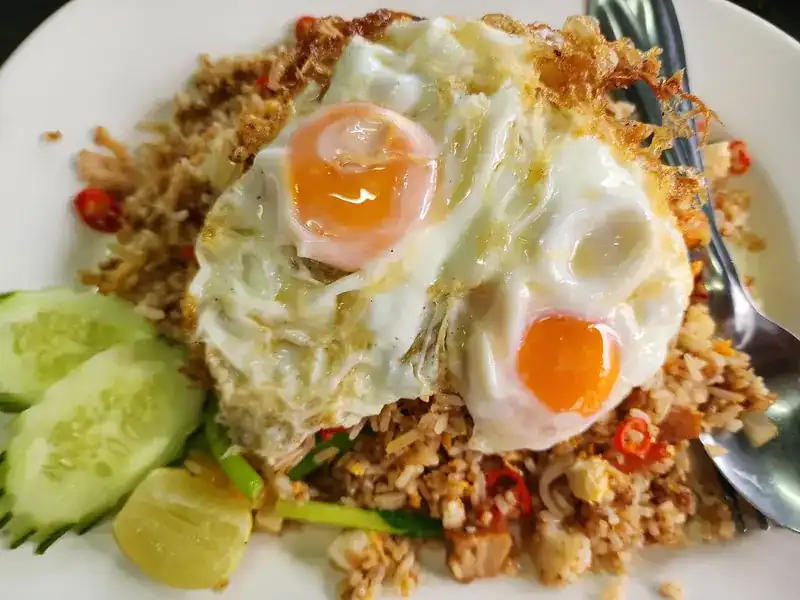 Fried rice with chilli, topped with two fried eggs, with cucumber and lime