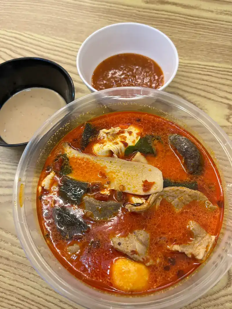 Red mala soup in a clear bowl with two dipping sauces