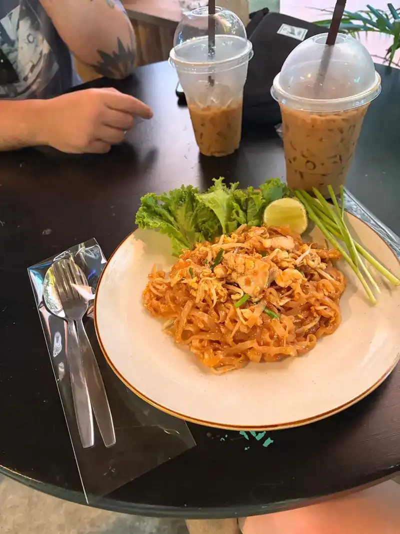 Pad thai with two iced drinks on a dark table