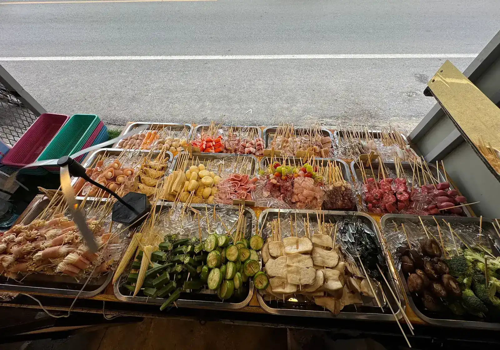 Steel trays of skewers on ice at the front of the stall, with the road just behind