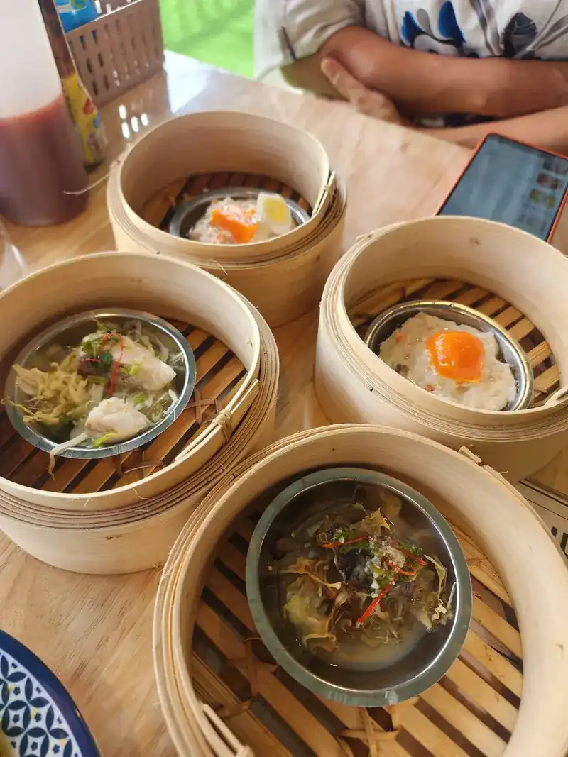 Four bamboo steamers on the table, each holding a steel cup of dim sum