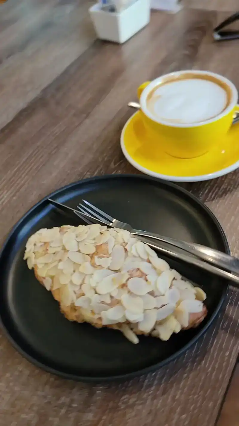 Almond croissant on a black plate with a hot coffee in a yellow cup