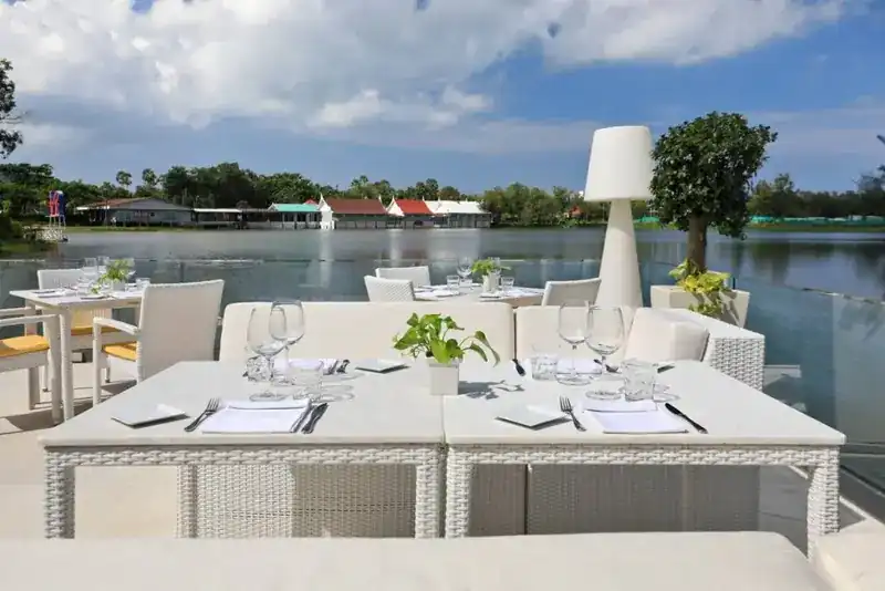 White tables set for lunch on the terrace, the lake and blue sky behind