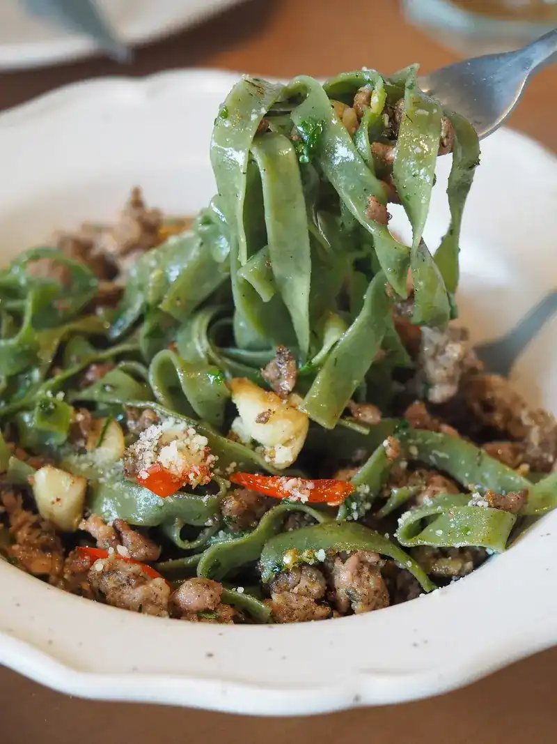 Green ribbon pasta with minced meat, garlic and chilli, lifted on a fork