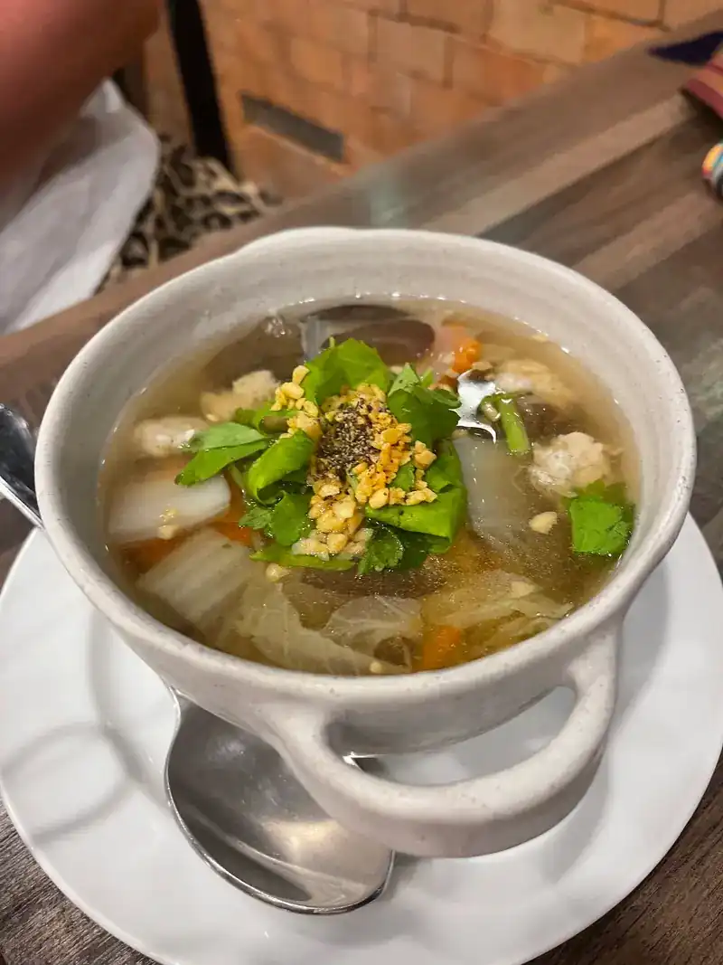 A bowl of clear Thai soup with glass noodles, cabbage, fried garlic and coriander