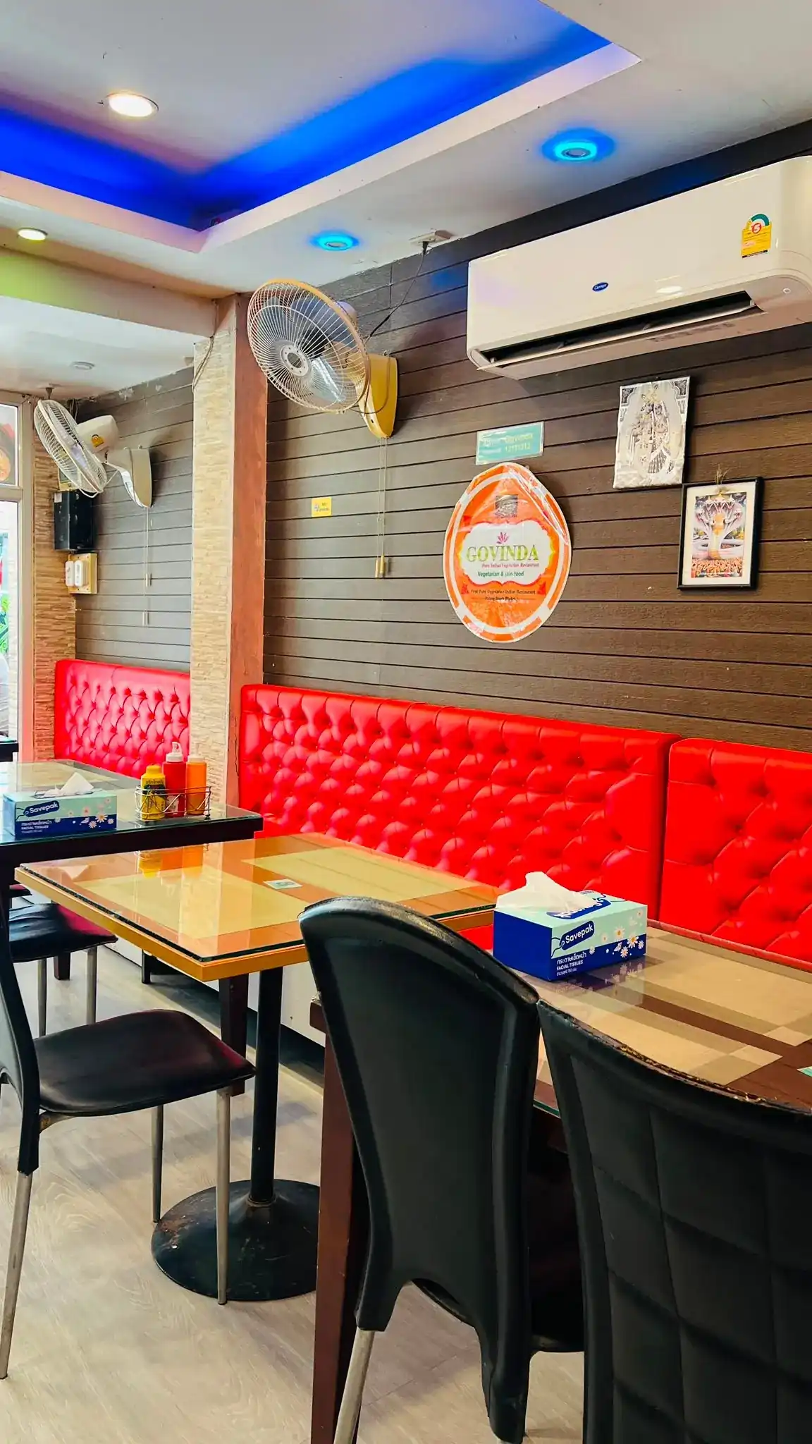 The red buttoned bench and the round Govinda sign on the dark slat wall