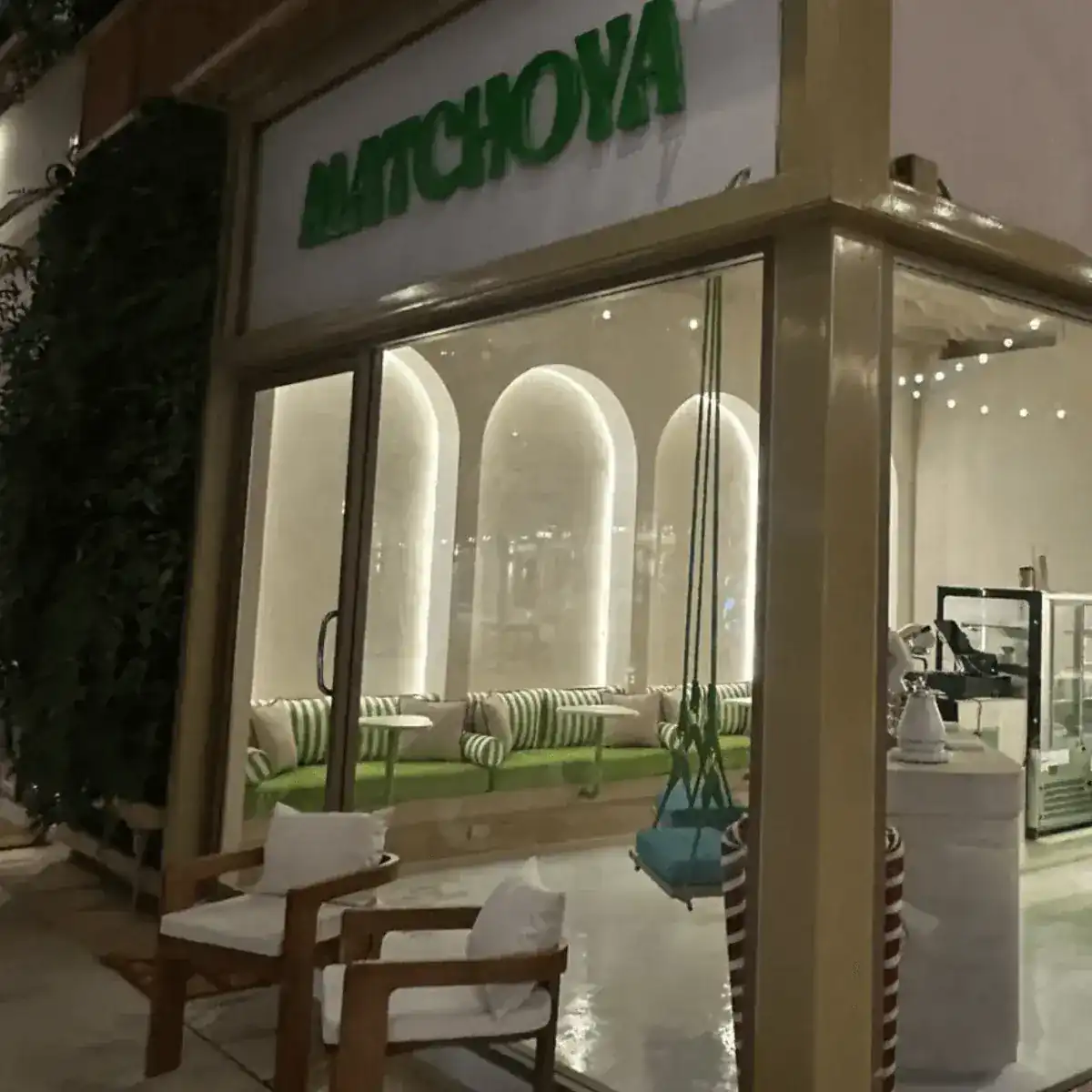 Matchoya's shopfront at Blue Tree Phuket in the evening: white arches inside, green striped benches and a rope swing by the window