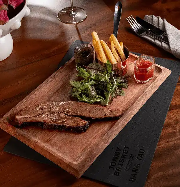 Sliced smoked brisket on a wooden board with fries, salad and chimichurri