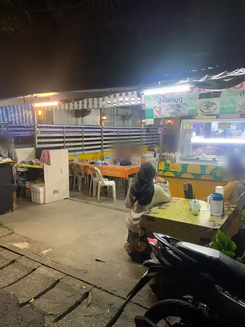 The open-air dining room at night: tables with orange cloths, plastic chairs and a lit food counter