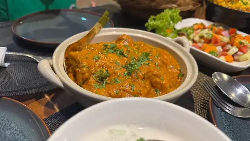 A curry in a white pot, with a bowl of chopped salad behind