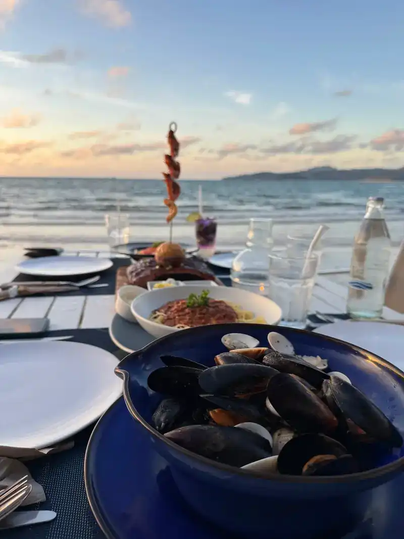 A bowl of mussels and a skewer on a table by the sea in the evening