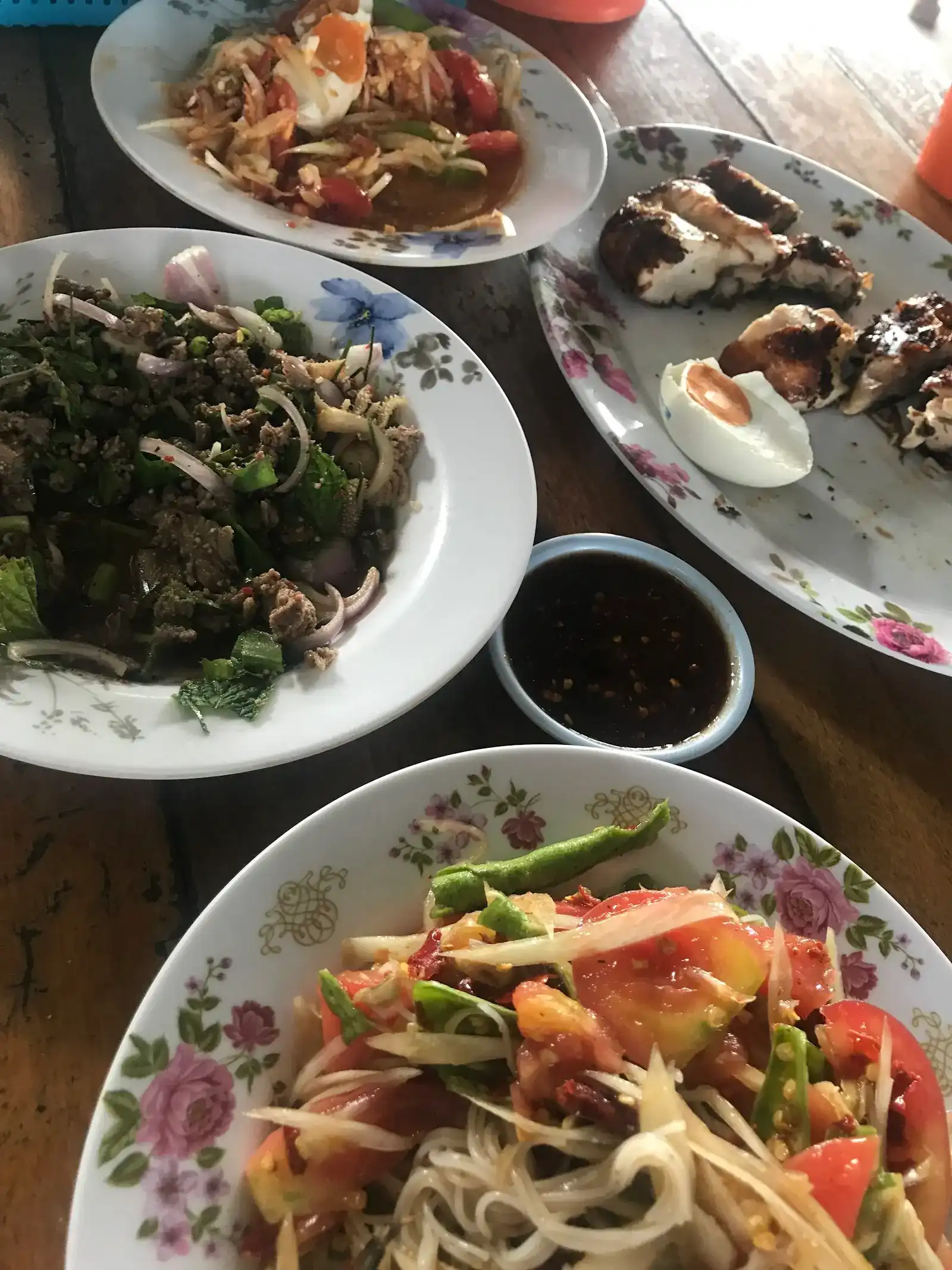 Papaya salad, a minced-meat salad with mint, grilled chicken with half an egg and a bowl of dipping sauce on flowered plates