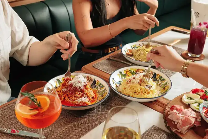 Spaghetti in hand-painted bowls at a table beside the green banquette