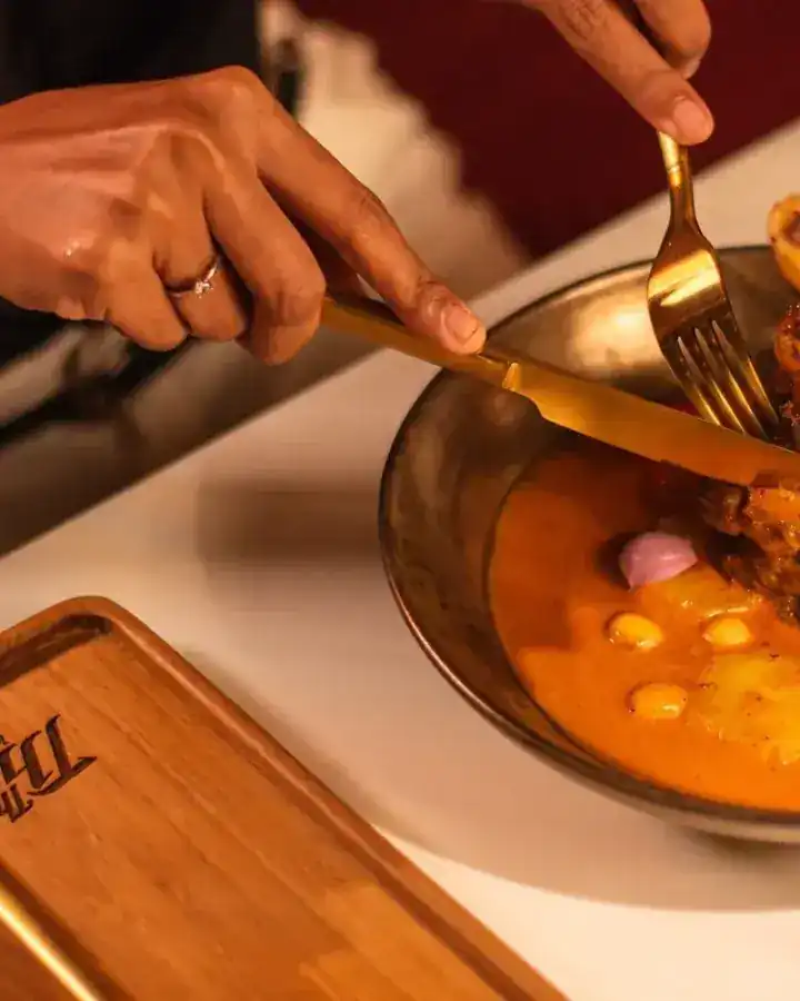 Hands with a golden knife and fork over a bowl of curry