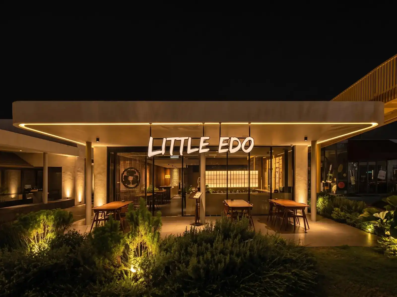 Little Edo at night: the lit sign under a long glowing eave, tables on the terrace, a garden in front
