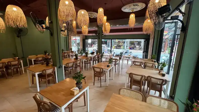 The dining room by day: green walls, rattan lanterns, wooden tables and wall fans, open to the street