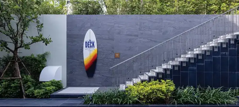 The Deck Beach Club surfboard sign on a slate wall beside a staircase