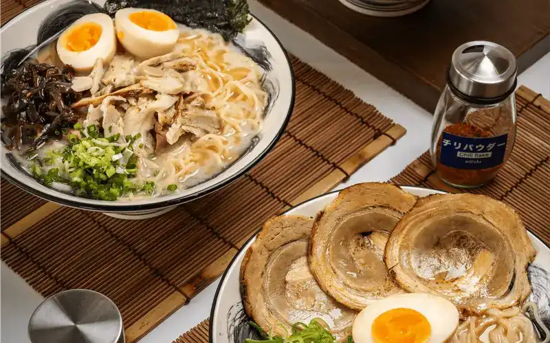 Ramen with shredded chicken beside a plate of rolled chashu and egg