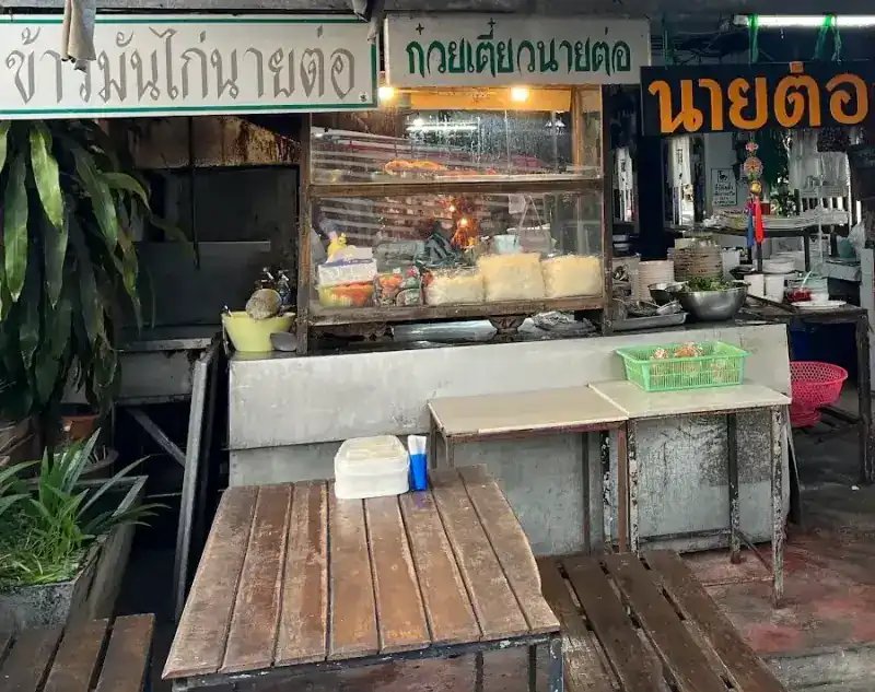 The stall under its signs for Nai Tor chicken rice and Nai Tor noodles, a glass noodle cabinet and wooden tables in front