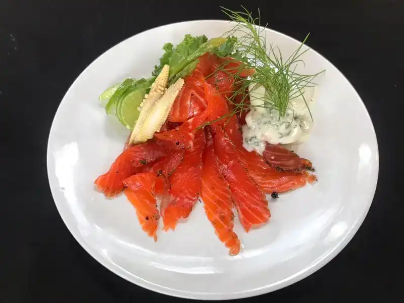 Salmon slices with dill, lime, baby corn and a creamy herb dip on a white plate