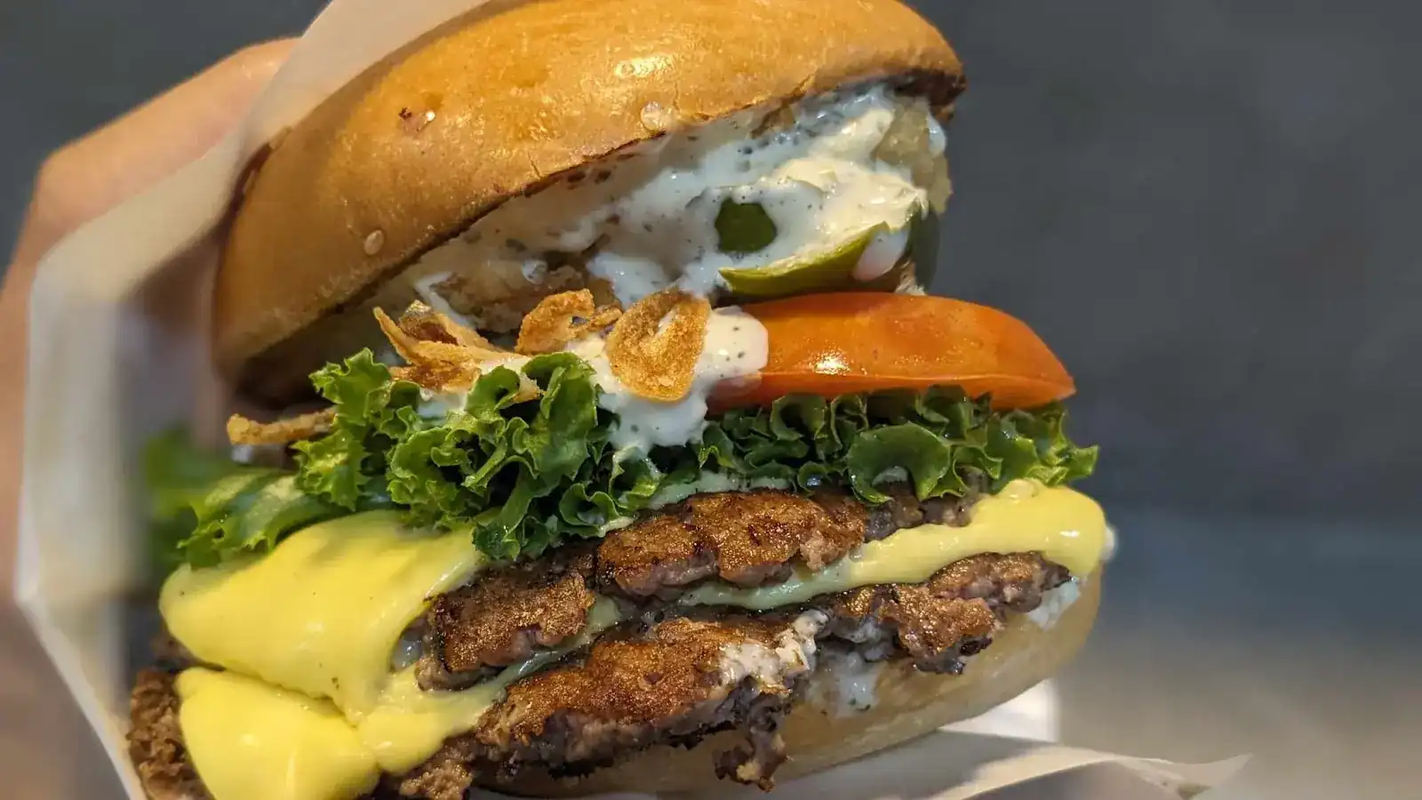 Beef burger with two thin patties, melted cheese, lettuce, tomato, fried onions and a creamy sauce, held in a paper wrap