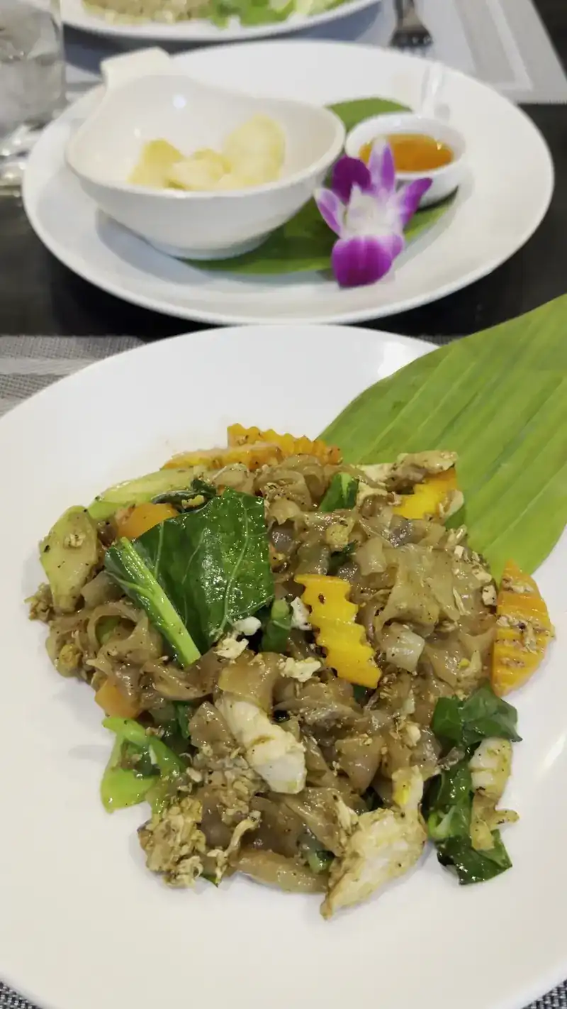 Stir-fried wide rice noodles with greens on a white plate