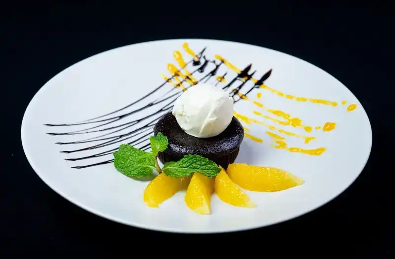 Chocolate cake with a scoop of ice cream, orange segments and mint on a white plate