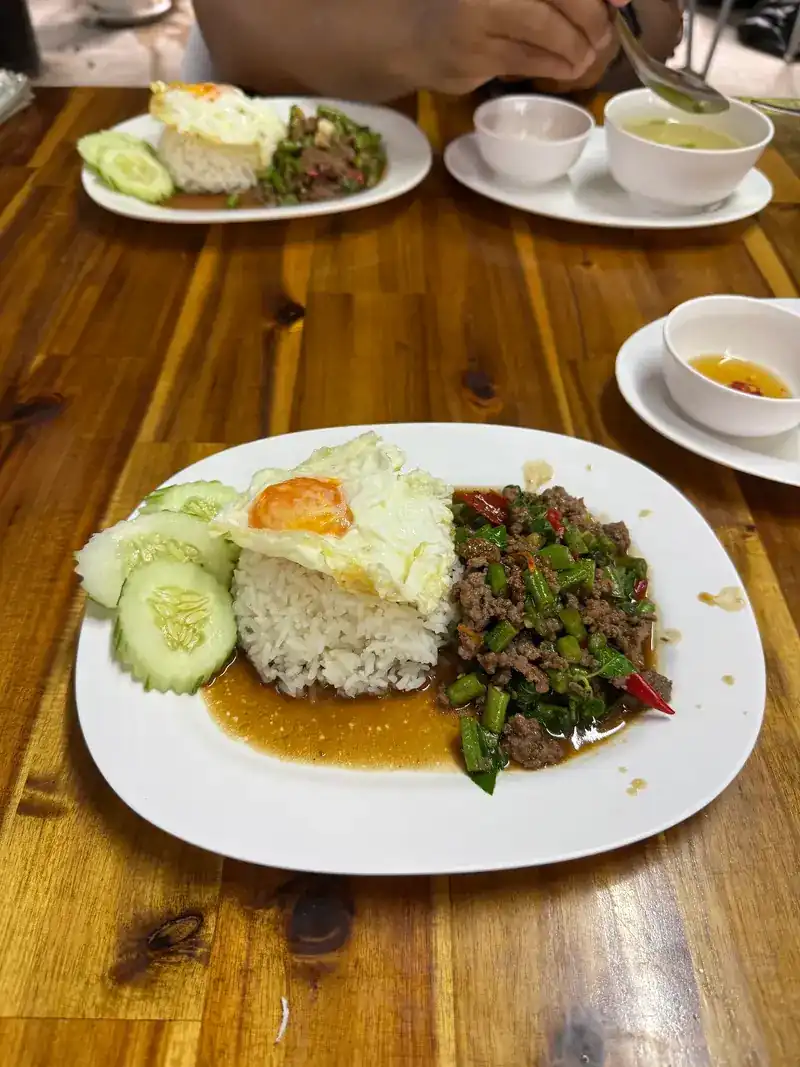 A stir-fry of minced meat, long beans and chilli over rice, with a fried egg and cucumber
