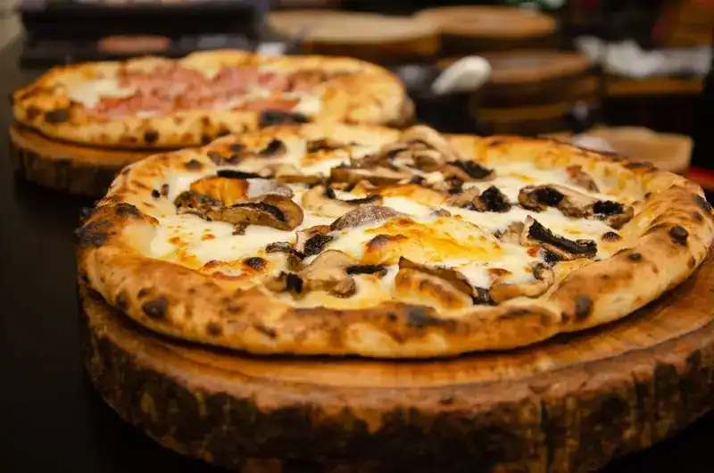 White pizza with mushrooms on a wooden board, a ham pizza behind it