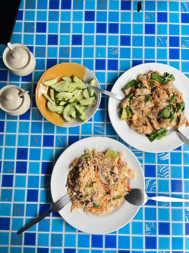 Stir-fried noodles with greens and a plate of fried rice on a blue tiled table