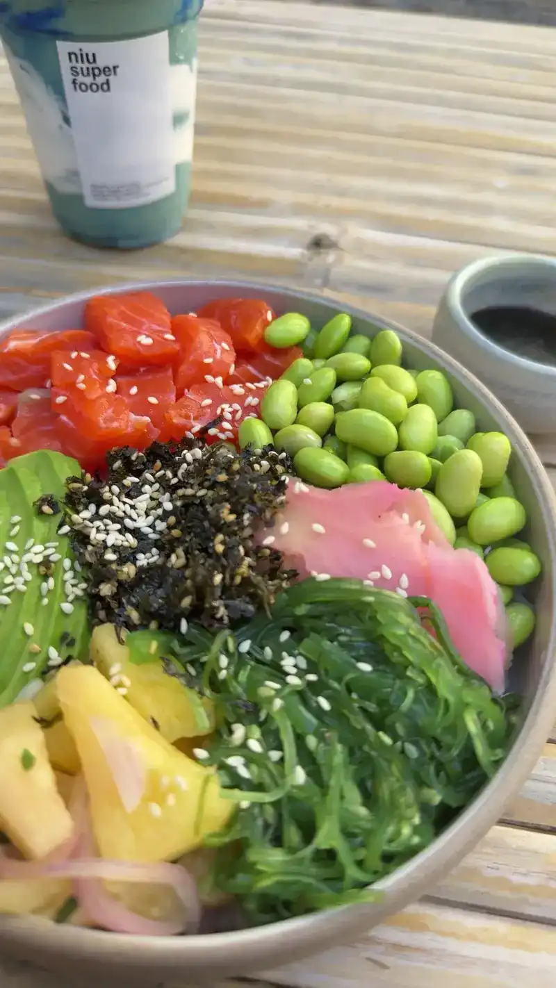 Poke bowl with edamame, seaweed and pineapple, with a Niu smoothie cup behind it